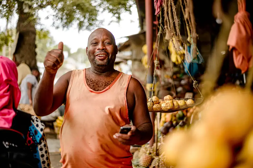 Commerçant souriant, téléphone à la main, devant son étal de fruits