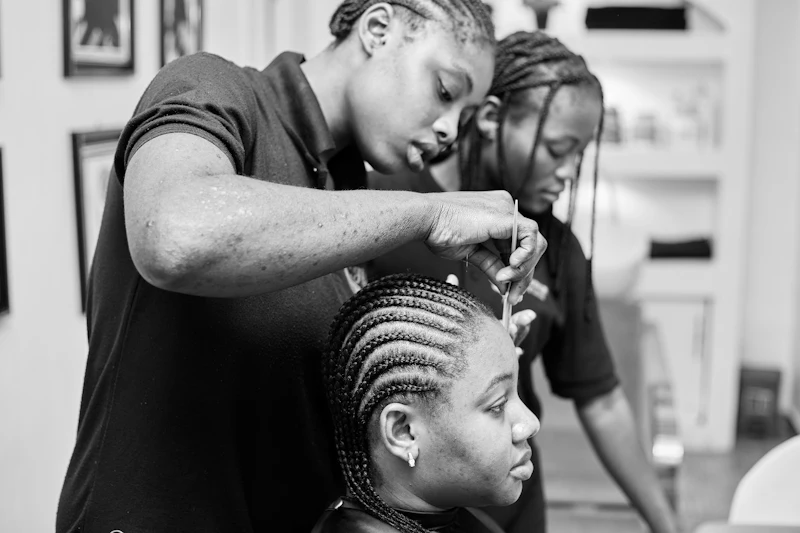Deux coiffeuses tressent les cheveux d'une cliente