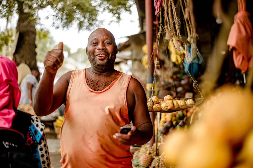 Commerçant souriant, téléphone à la main, devant son étal de fruits